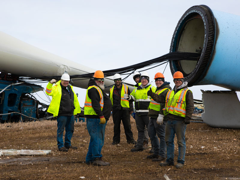 group of men in hard hats in front of wind turbine being disassembled